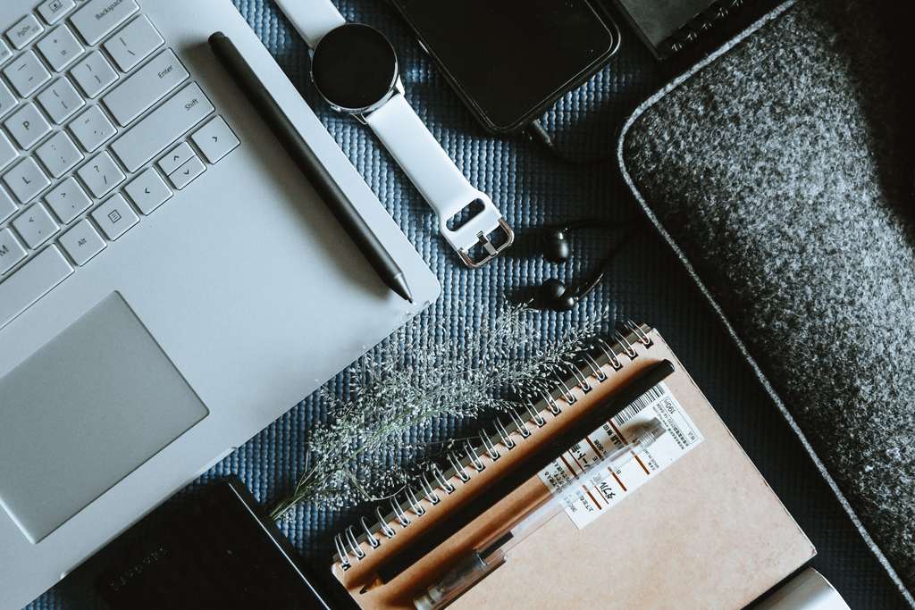 Vue de dessus d’un bureau : ordinateur portable, montre connectée, écouteurs et carnet à spirale