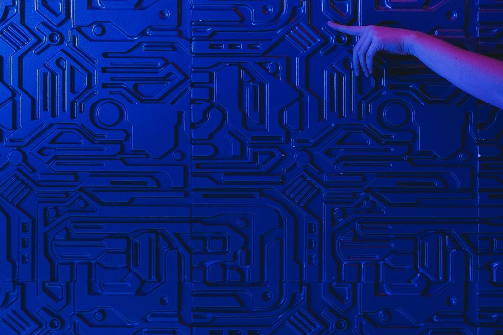 Un doigt effleure un circuit imprimé bleu, sous une lumière violette