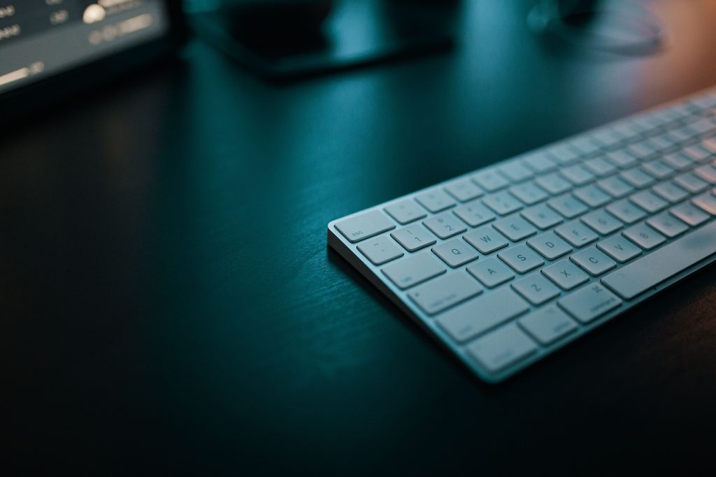A white keyboard on a dark desk, lit from the side