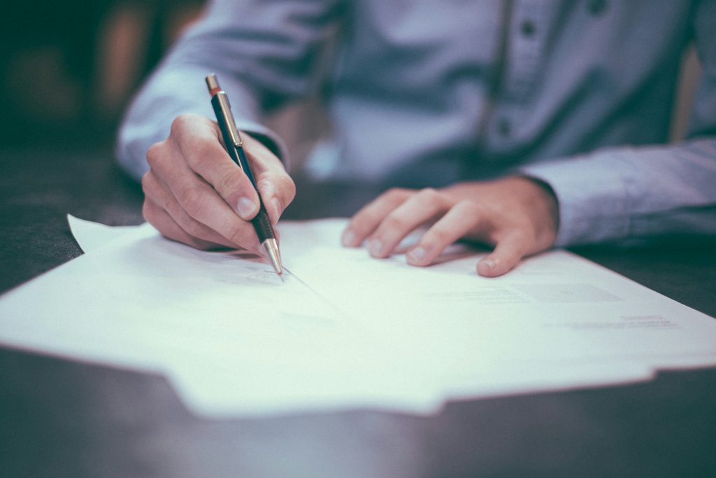 A hand writing in pencil on a blank sheet of paper on a desk