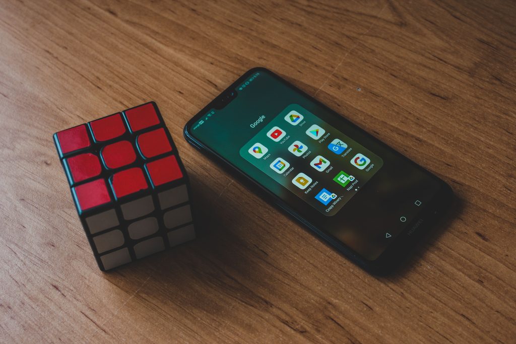 A Rubik’s cube beside a smartphone on a wooden table, seen from above