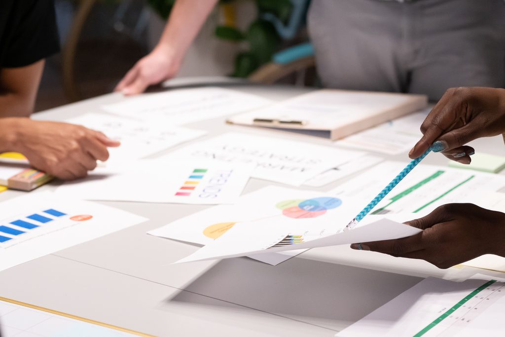 Plusieurs mains disposent sur une table blanche des feuilles imprimées de graphiques colorés