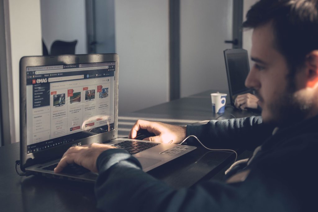 Un homme consulte sur un ordinateur portable une page faite de vignettes, dans un bureau sombre