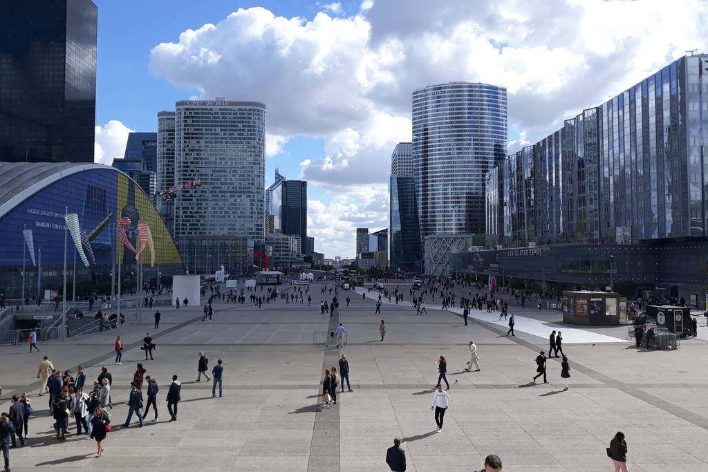 Une esplanade urbaine où marchent des passants dispersés, bordée de tours de bureaux