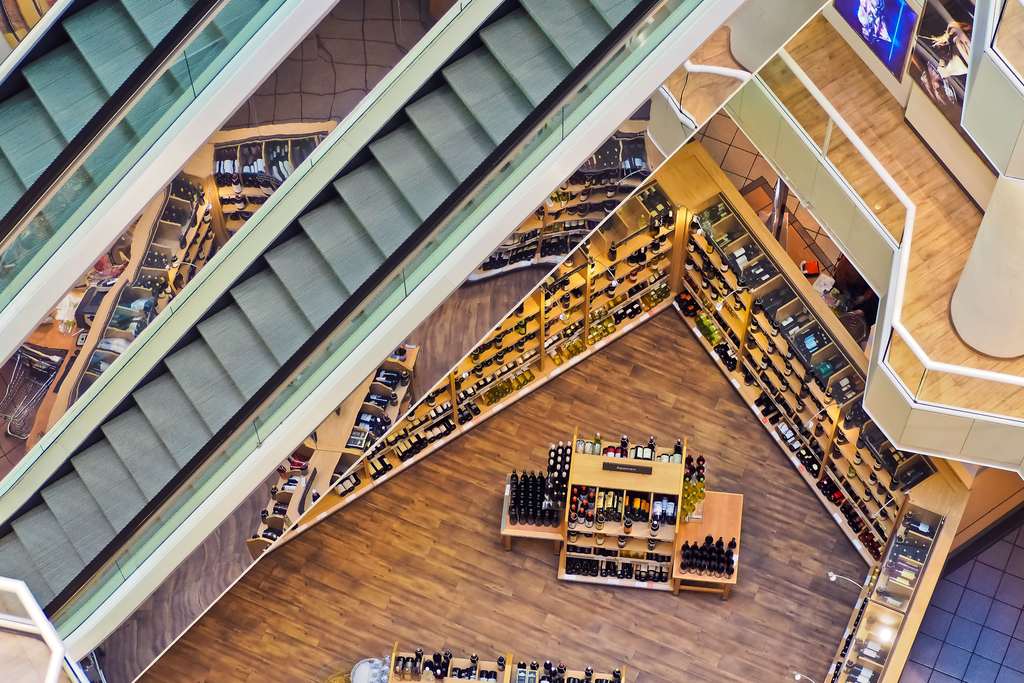 Vue plongeante sur plusieurs niveaux d’une galerie marchande traversée par des escalators
