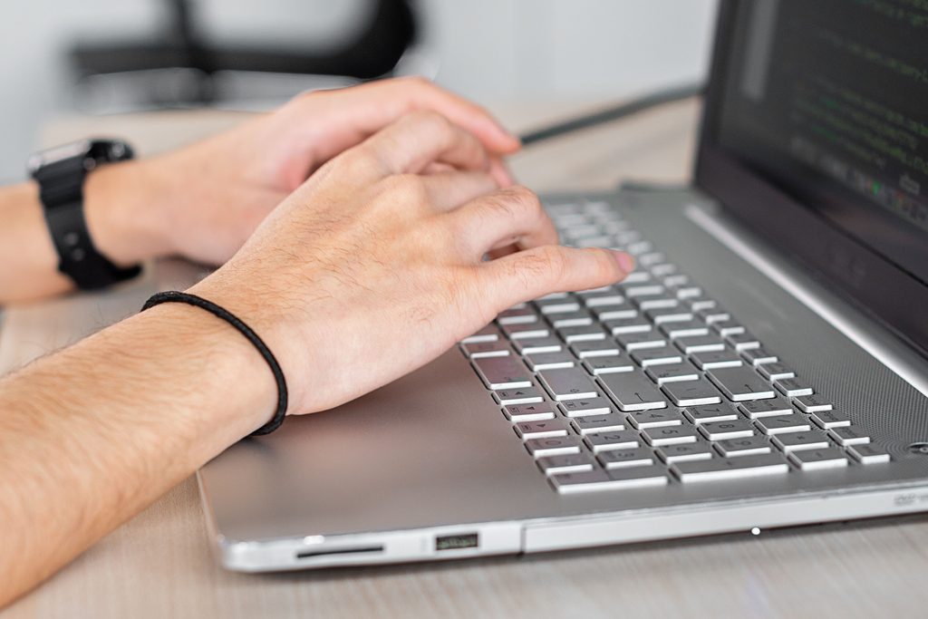 Les mains d’une personne sur le clavier d’un ordinateur portable affichant du code