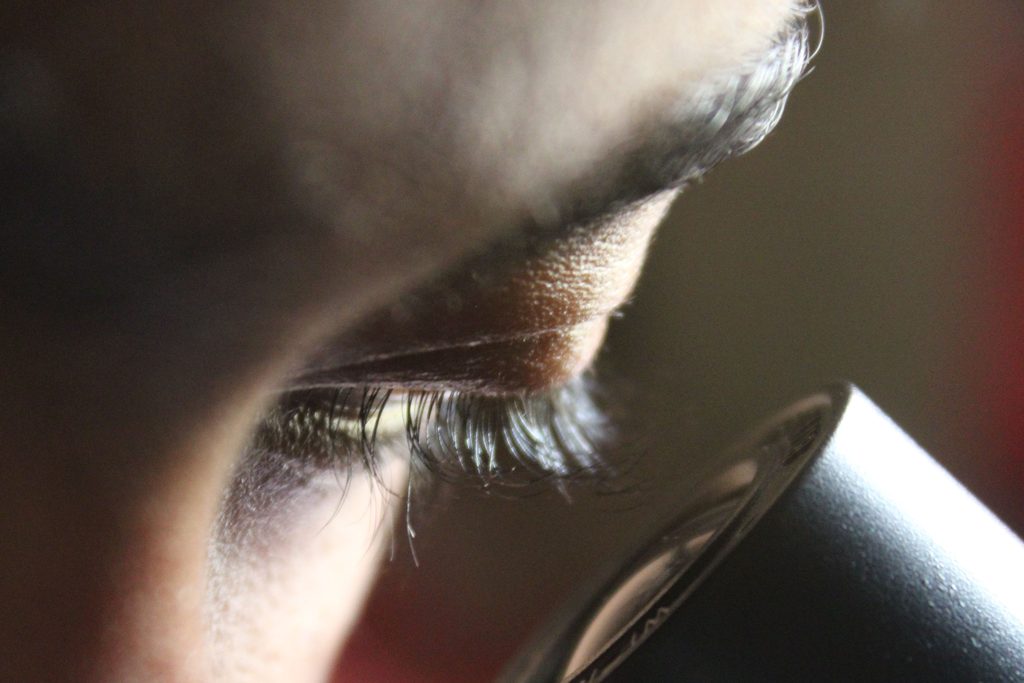 Une personne penchée sur l’oculaire d’un microscope, le visage éclairé d’une lumière rouge