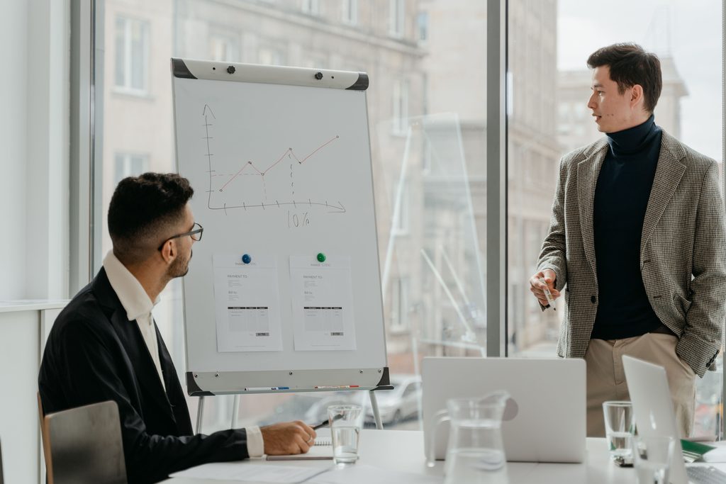 Two people meeting in front of a flip chart showing a curve and two indicators