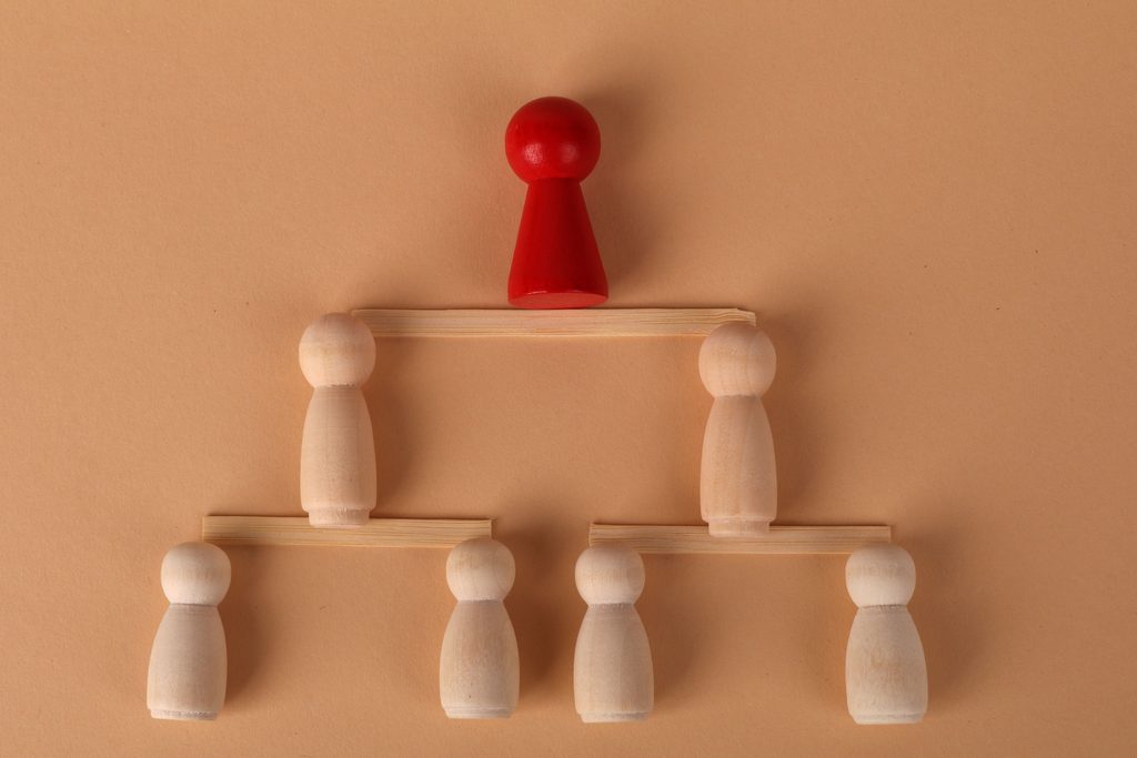 Des pions en bois disposés en organigramme sur trois niveaux, celui du sommet peint en rouge