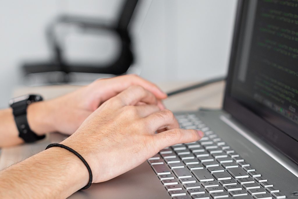 Deux mains sur le clavier d’un ordinateur portable, un casque audio posé à côté