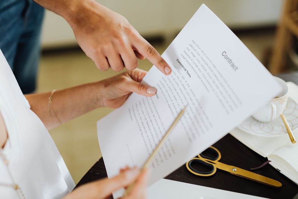 Deux personnes relisent un contrat imprimé ; l’une pointe du doigt un paragraphe intitulé « Commercial Terms »