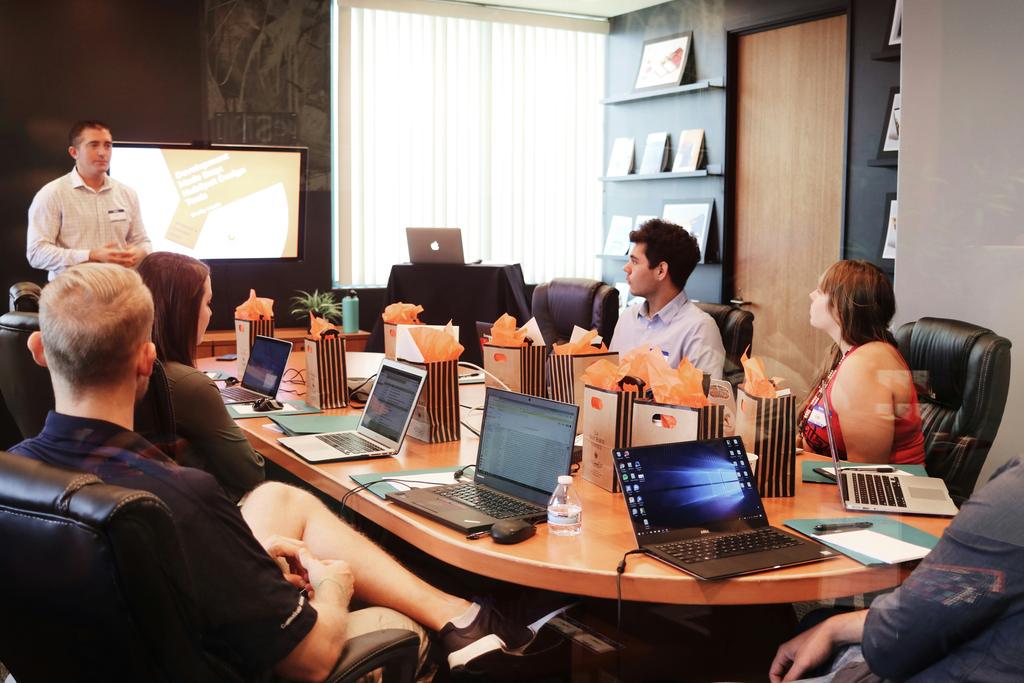 A team meeting around a large table, a speaker standing in front of a screen