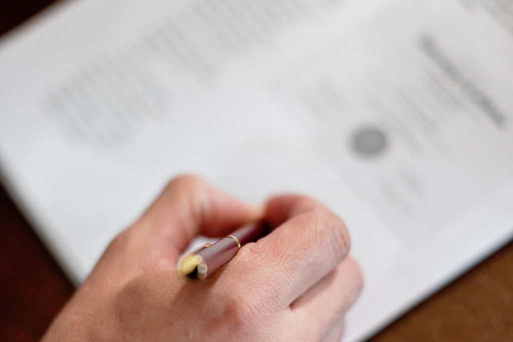 Une main écrit au stylo sur un document imprimé, posé sur une table en bois