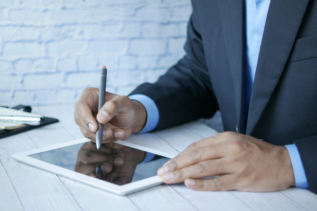 Un homme en costume écrit au stylet sur une tablette posée devant lui