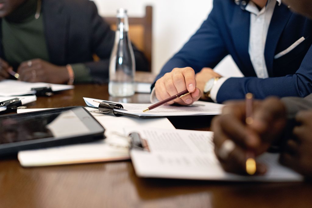 Autour d’une table de réunion, plusieurs personnes annotent des documents ; une tablette est posée à côté