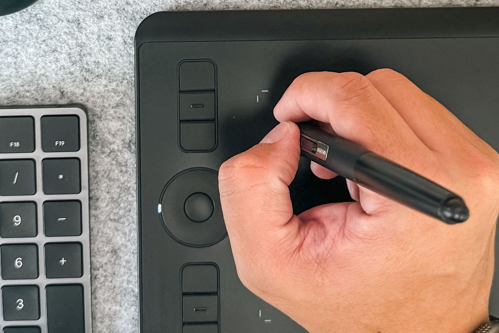 Vue de dessus d’une main tenant un stylet sur une tablette graphique, à côté d’un clavier
