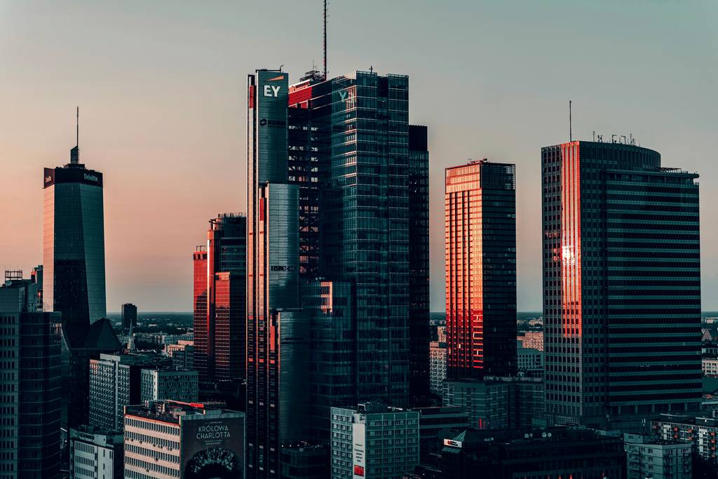 Des tours de bureaux au crépuscule, leurs façades vitrées teintées de rouge par le soleil couchant