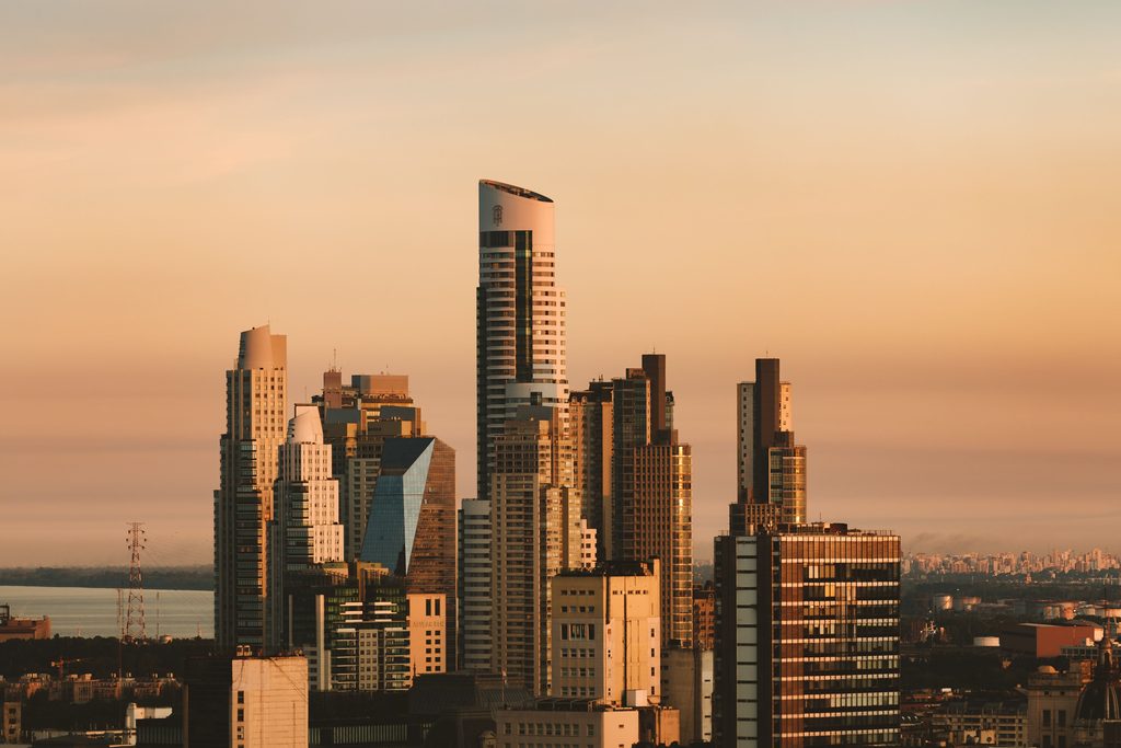 Des tours de bureaux se détachent sur un ciel orangé, au-dessus d’une ville au crépuscule